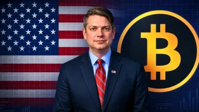 Nick Begich in a suit and tie standing between the United States flag and a large glowing Bitcoin logo on a blue digital grid background.