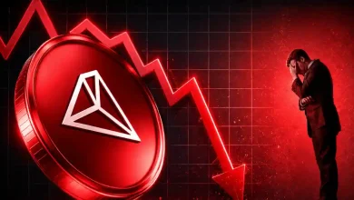 Large red TRON token next to a falling neon red arrow and a stressed businessman holding his head on a dark gridded background.