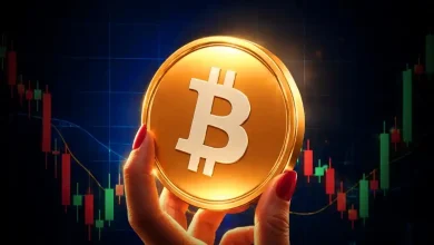 A hand with red nails holding a large golden Bitcoin coin against a candlestick chart.