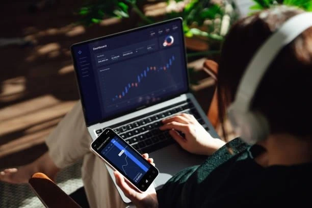 A woman watching charts on laptop and mobile.