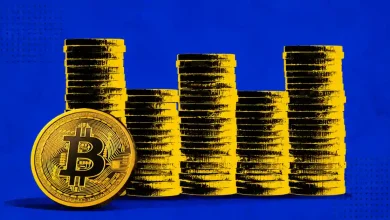 Gold Bitcoin coin leaned against stacked gold coins on a blue background.